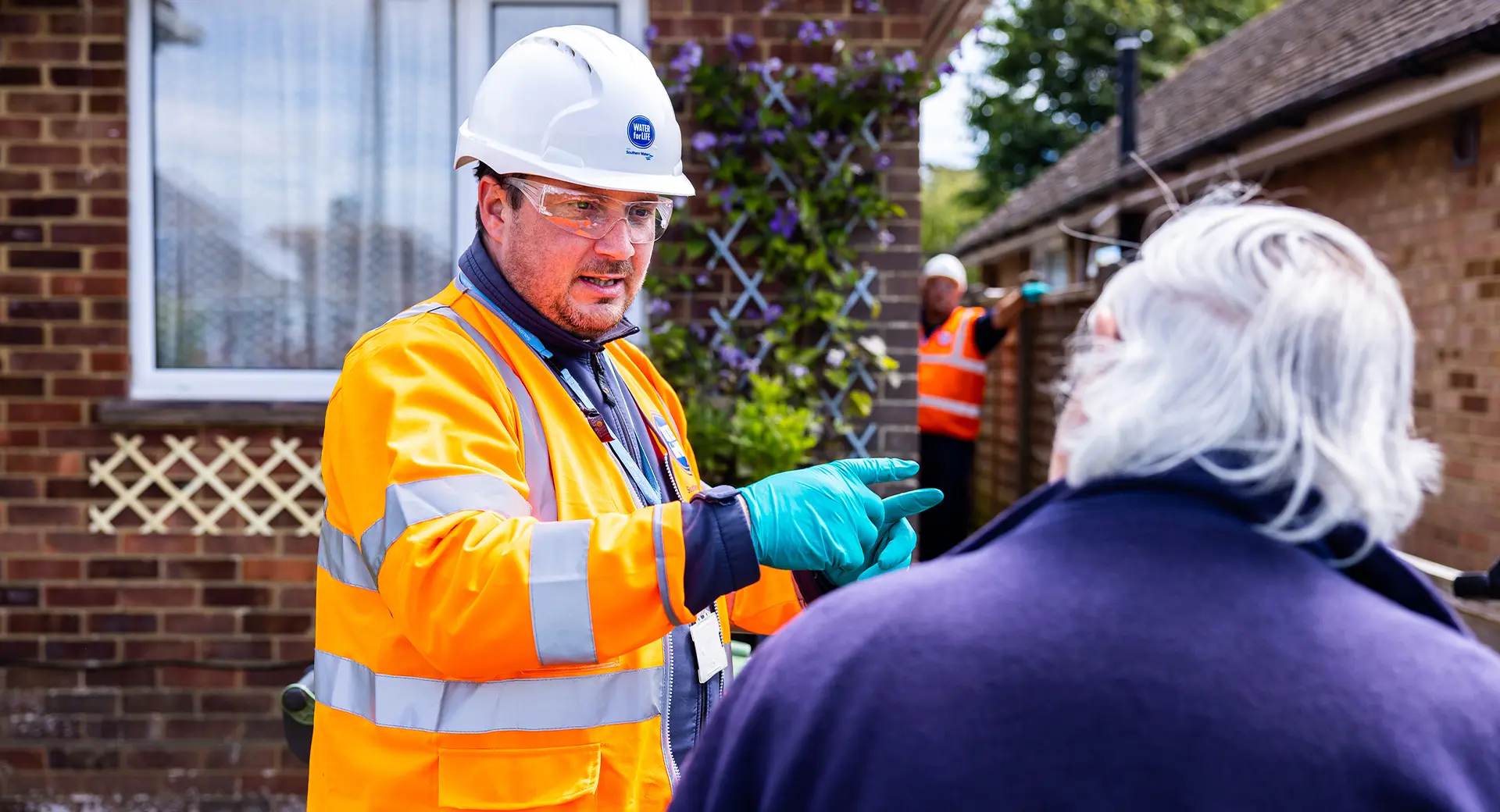 A Southern Water engineer talks to a customer in their garden with another employee visible in the background
