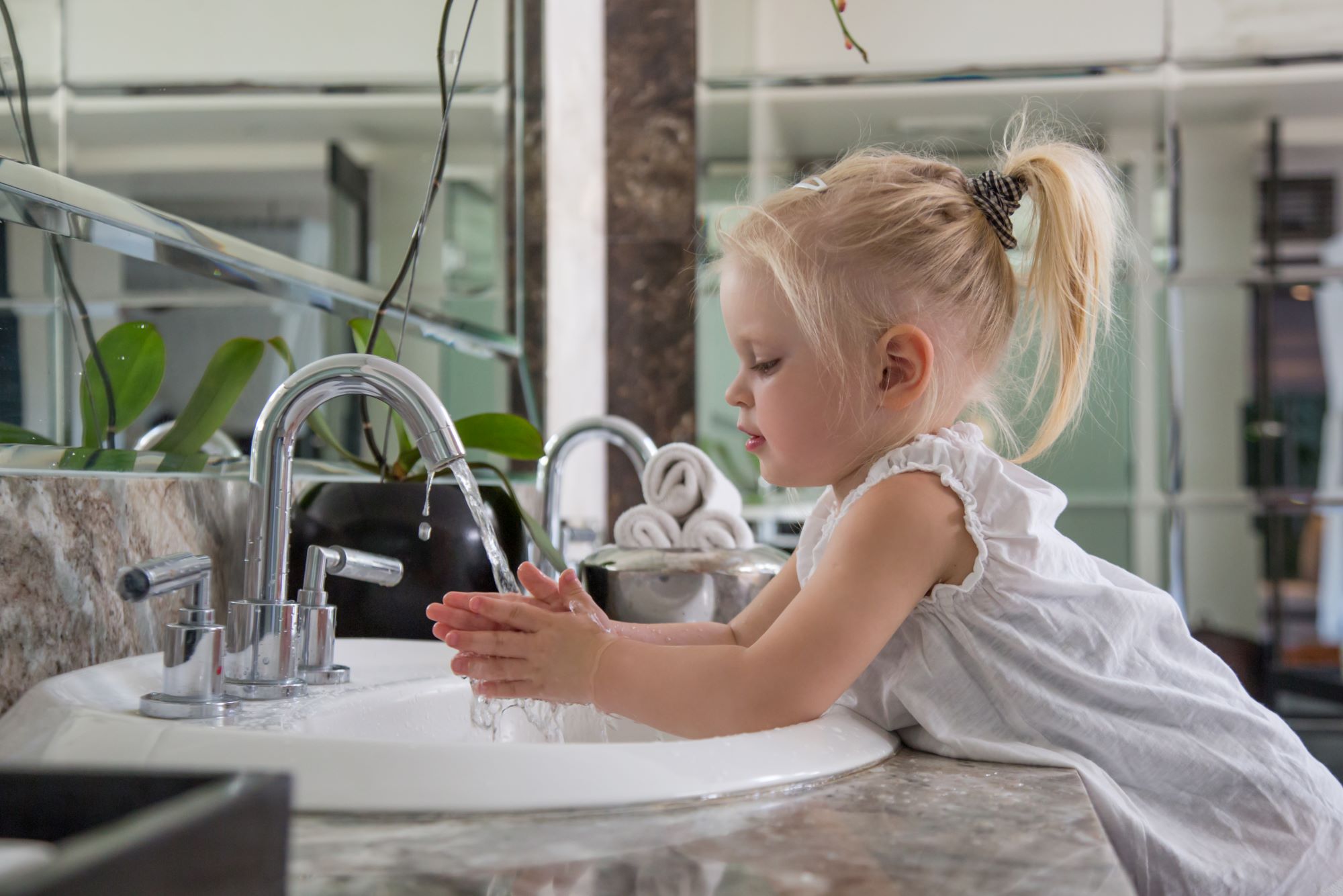young child washing hands at bathroom sink
                        