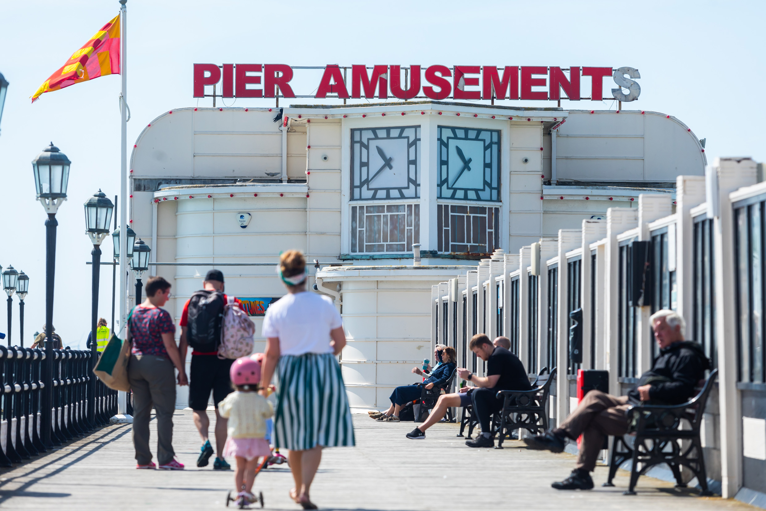 People walk along Worthing Pier on a sunny day