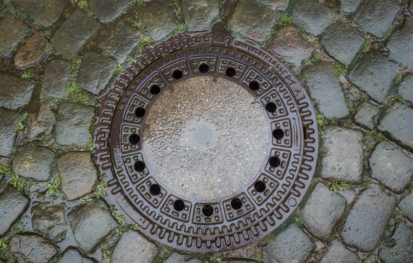 A manhole cover in a rainy cobbled street