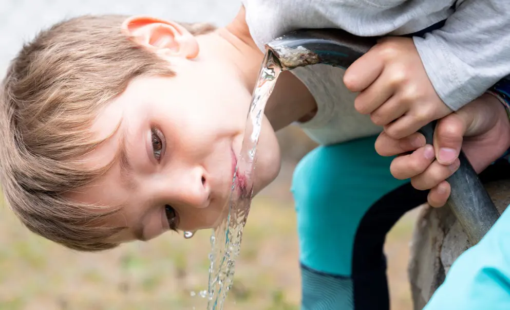 A close-up of a child drinking water straight from an outdoor tap on a bright day