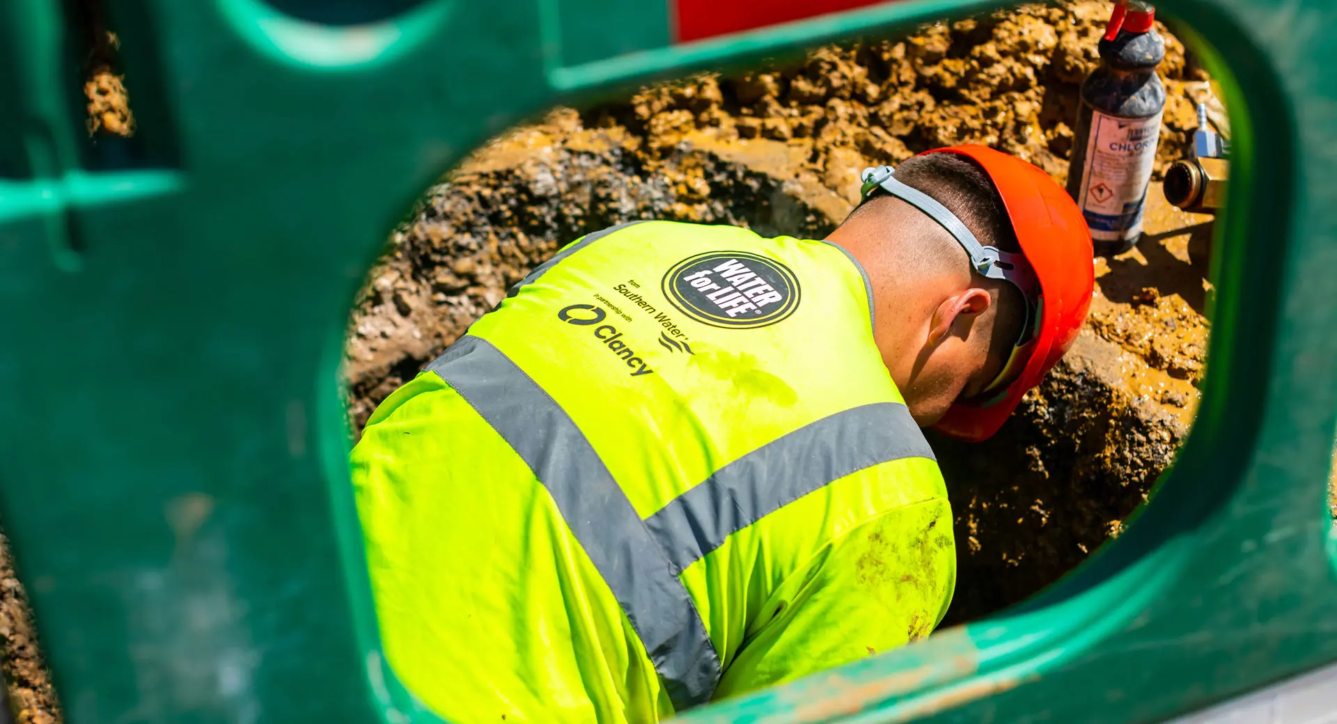 A close-up of a plastic barrier. On the other side of the barrier, a Clancy Repair Team engineer works in an excavated area of ground