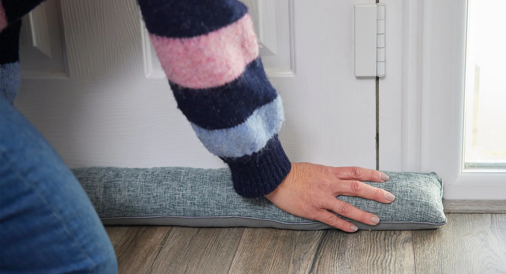 A person placing a draft excluder at the bottom of a door