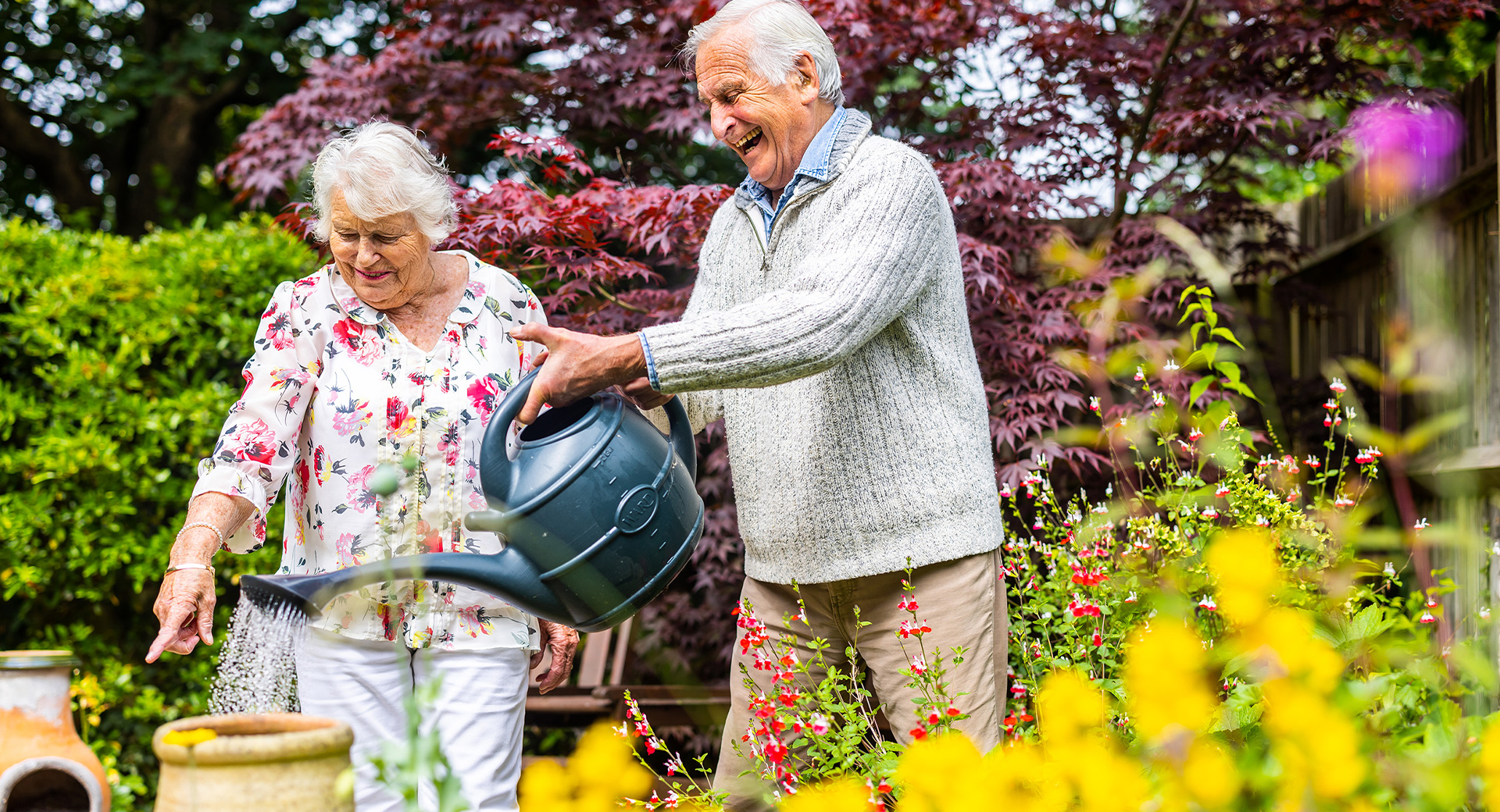 Elderly customers watering their garden with a watering can
                        