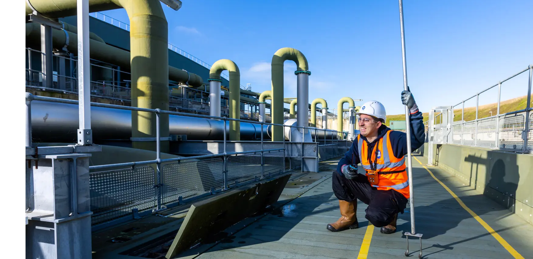A Southern Water engineer smiles and crouches next to pipes at a water treatment works
