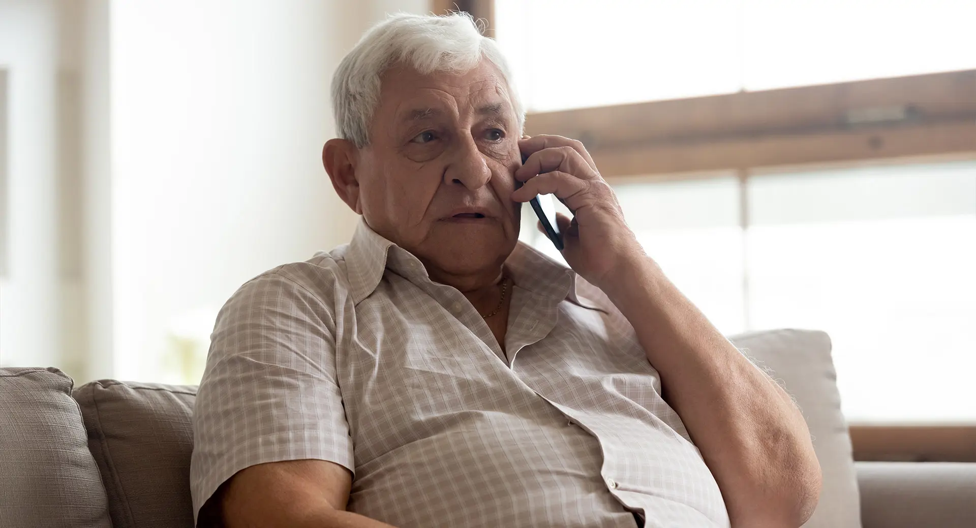 An older person holds a mobile phone up to their ear